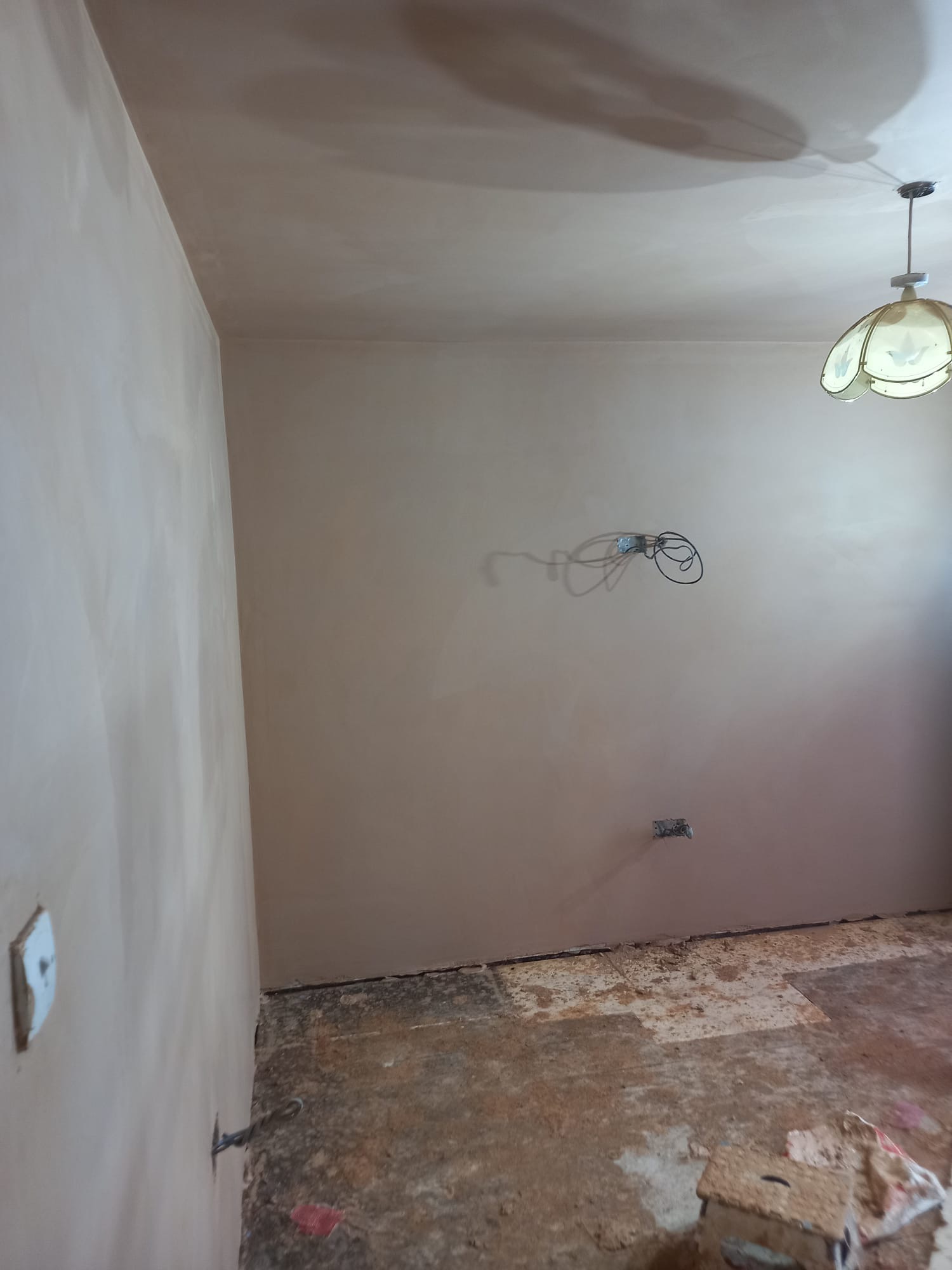 Pokój w trakcie prac wykończeniowych: świeżo położona gładź na ścianach i suficie, widoczne kable elektryczne wystające ze ściany, stare podłoże podłogowe, wisząca lampa z kloszem w stylu retro.