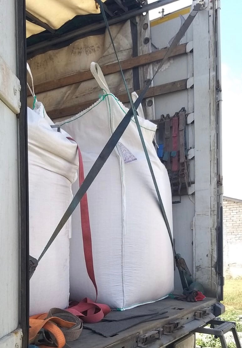 Wnętrze naczepy z dwoma dużymi workami typu Big Bag zabezpieczonymi pasami transportowymi, widoczne uchwyty worków i ściany naczepy.