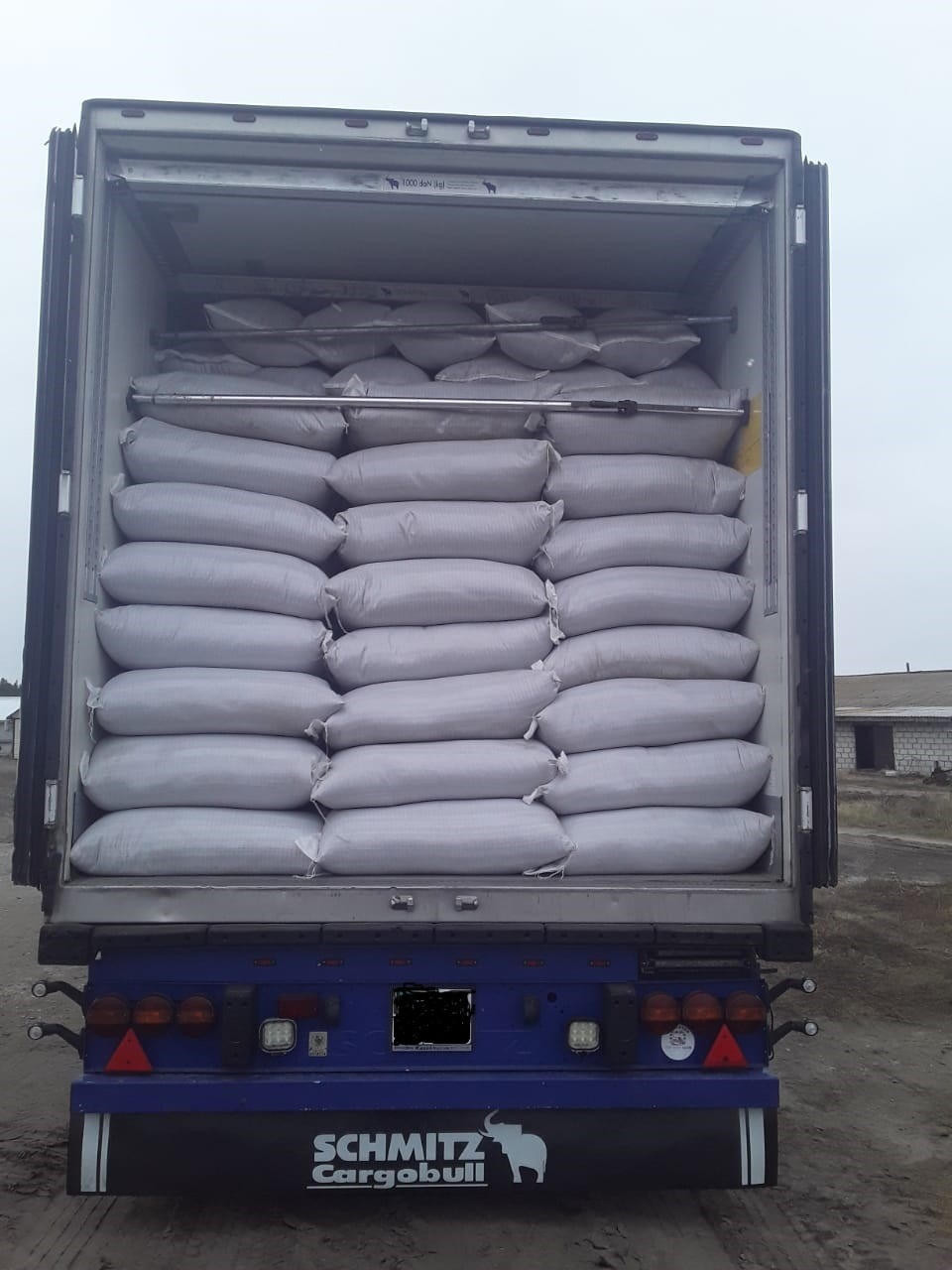 Otwarta naczepa ciężarówki załadowana workami, widok z tyłu, logo Schmitz Cargobull na dole.