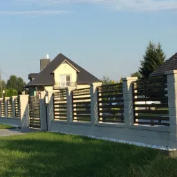 Nowoczesne ogrodzenie betonowe z metalowymi przęsłami w Rzeszowie, widoczne z zewnątrz posesji, z bramą wjazdową, na tle zadbanego trawnika i domu.