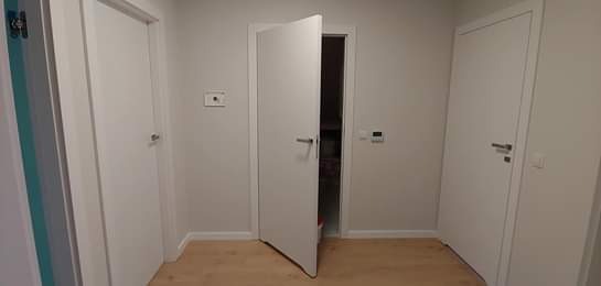 Trzy białe drzwi wewnętrzne w jasnym korytarzu, jedne z nich są otwarte, ukazując wnętrze pomieszczenia.