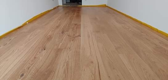 Świeżo położona, jasna podłoga z desek parkietowych, zabezpieczona taśmą malarską przy ścianach, widok z niskiej perspektywy.