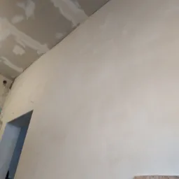 Ściana po tynkowaniu, widoczne ślady po łatach na suficie, przygotowanie do malowania, fragment płyty na podłodze.