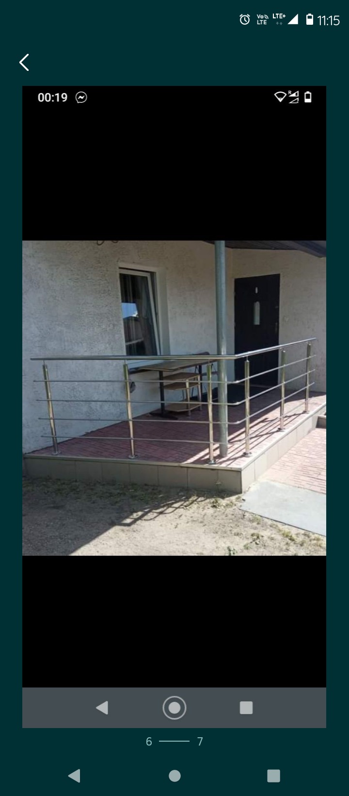 Nierdzewna balustrada przed wejściem do budynku z oknem i czarnymi drzwiami, widok z zewnątrz na taras wyłożony czerwoną kostką.