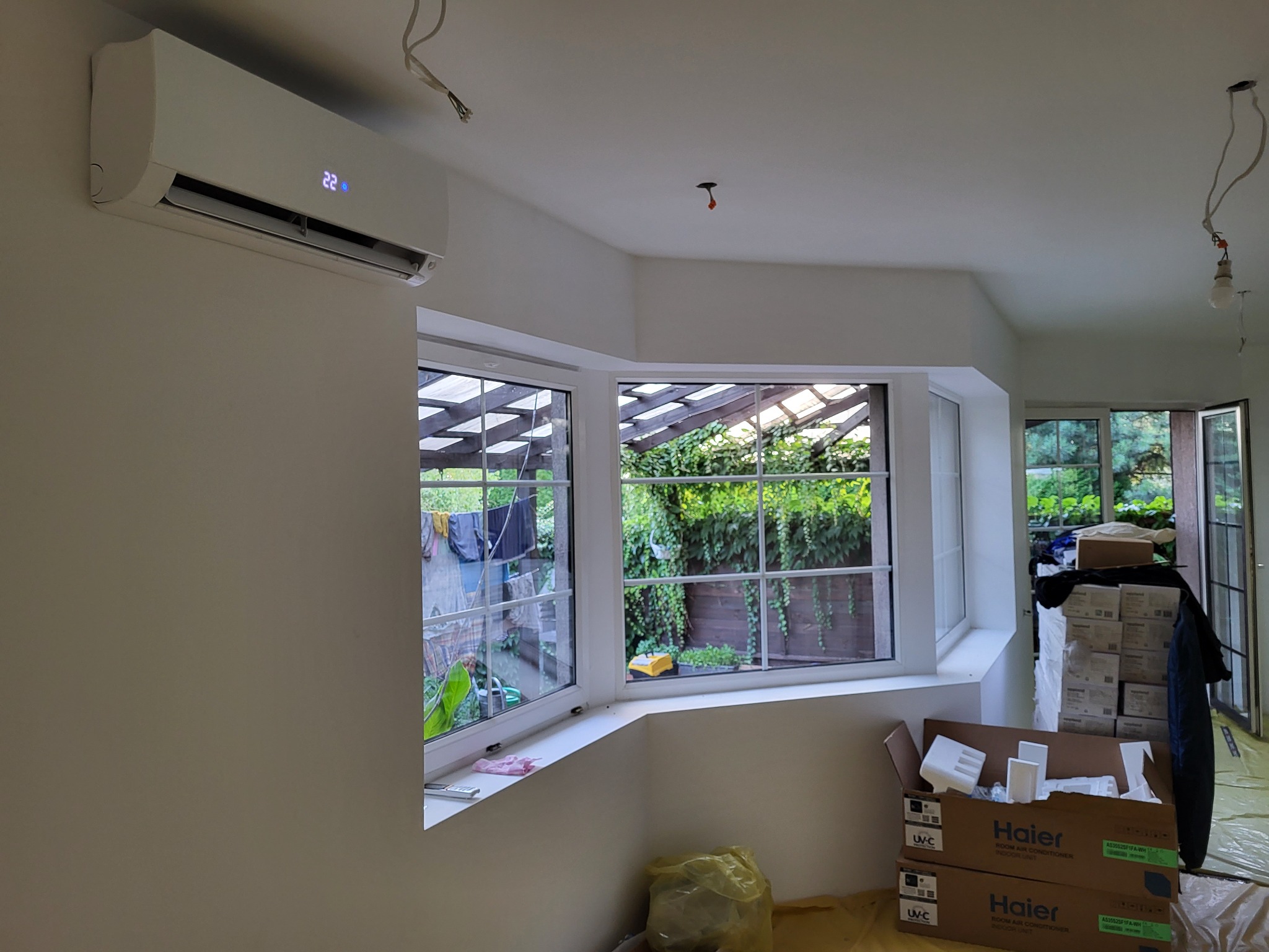 Biały klimatyzator Haier zamontowany na ścianie w jasnym pokoju z dużym oknem, widoczne kartony po klimatyzatorach i przygotowania do montażu.