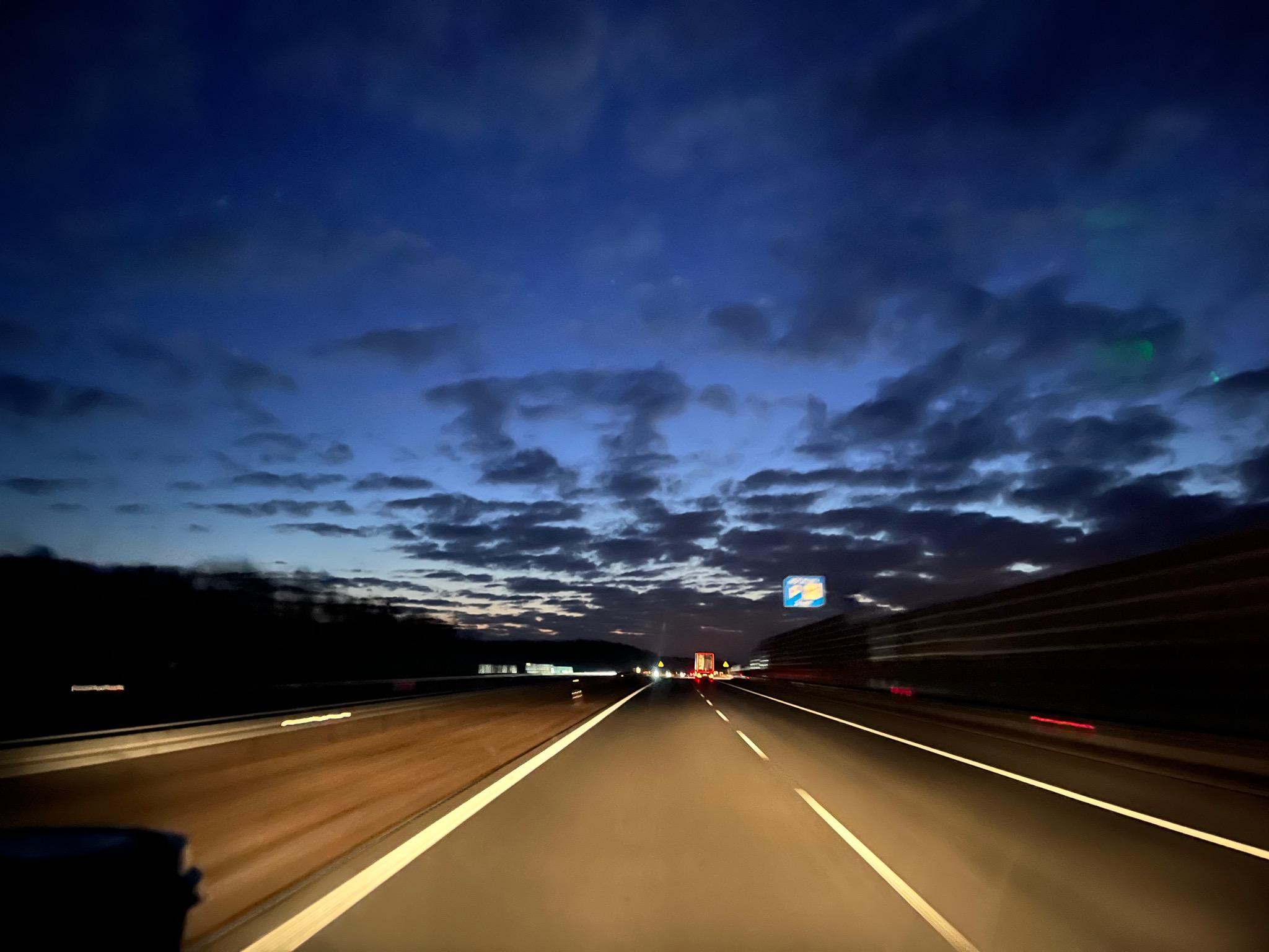 Nocny widok z kabiny kierowcy na autostradę w okolicach Augustowa, z widocznymi światłami innych pojazdów i zachmurzonym niebem nad drogą.