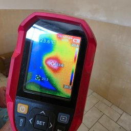 JN Hydro Usługi Instalacyjne - Termowizja ściany ukazuje rozkład temperatur na ekranie urządzenia, z datą 2025/07/26. Widoczna mozaika podłogowa i fragment ściany w tle.