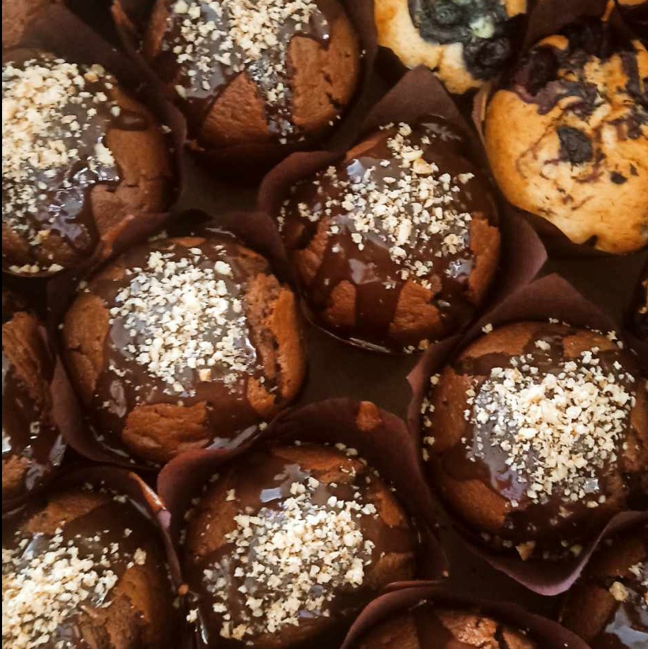 Widok z góry na czekoladowe babeczki w brązowych papilotkach, polane błyszczącą polewą i posypane kruszonką, obok babeczki z borówkami.