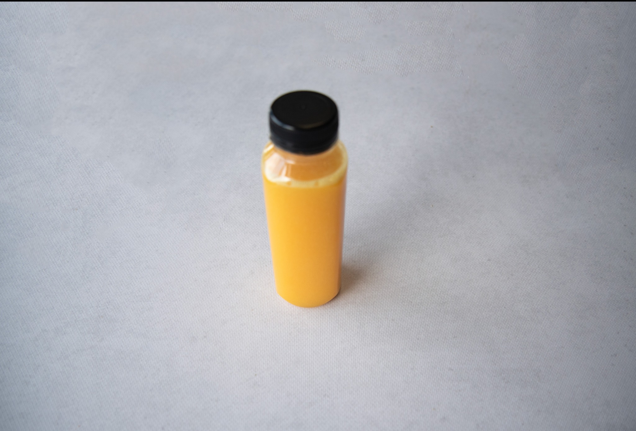 Butelka z pomarańczowym sokiem na szarym tle, czarna zakrętka, minimalistyczna kompozycja.