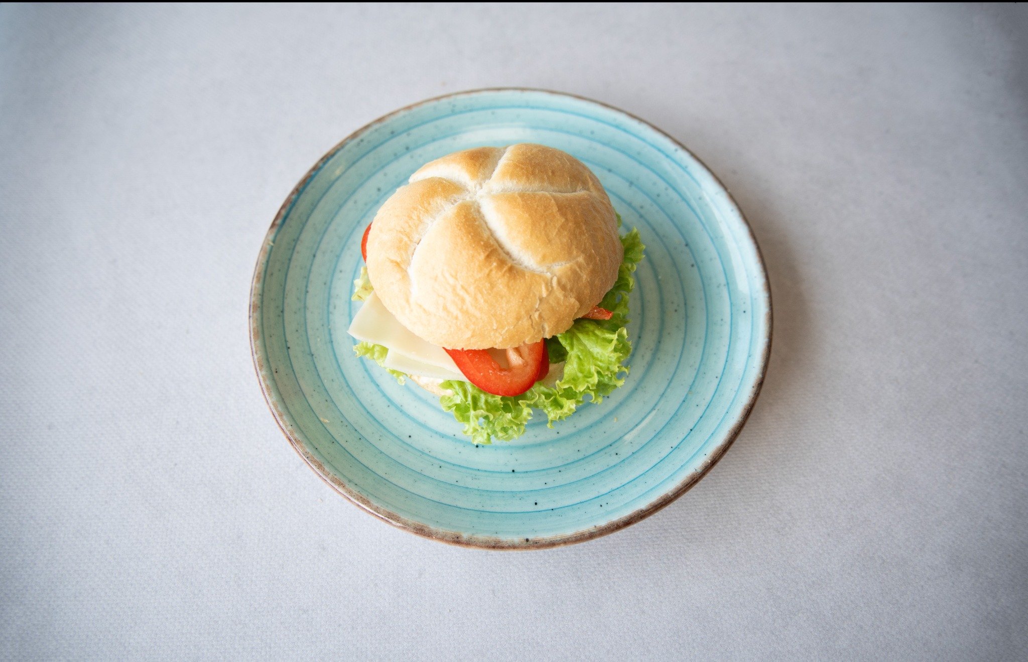 Kanapka z serem, pomidorem i sałatą na turkusowym talerzu z Rzeszowa, ujęcie z góry.