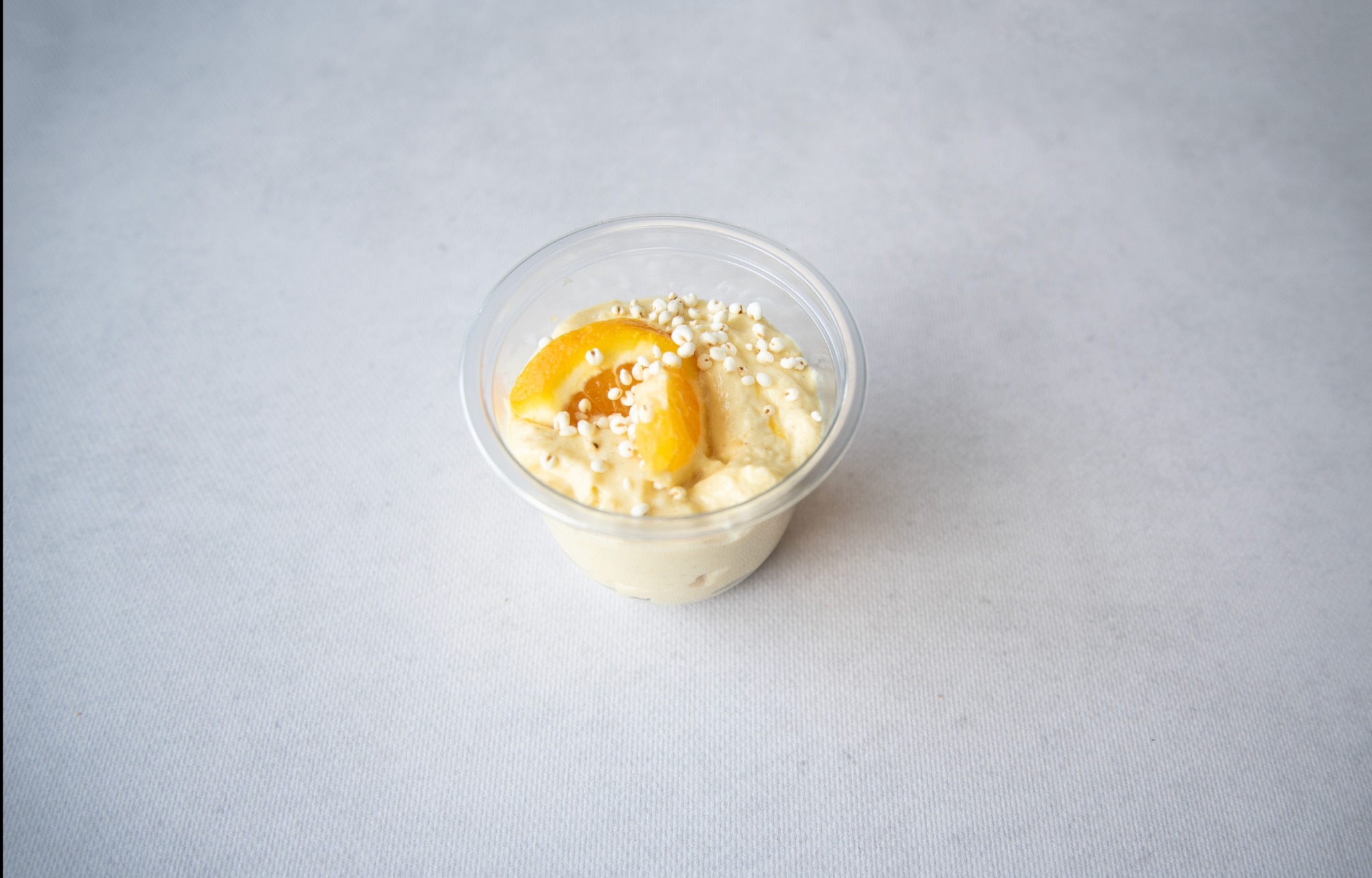 Deser w przezroczystym pojemniku, udekorowany plasterkami pomarańczy i posypką z białych kuleczek, na jasnym tle.
