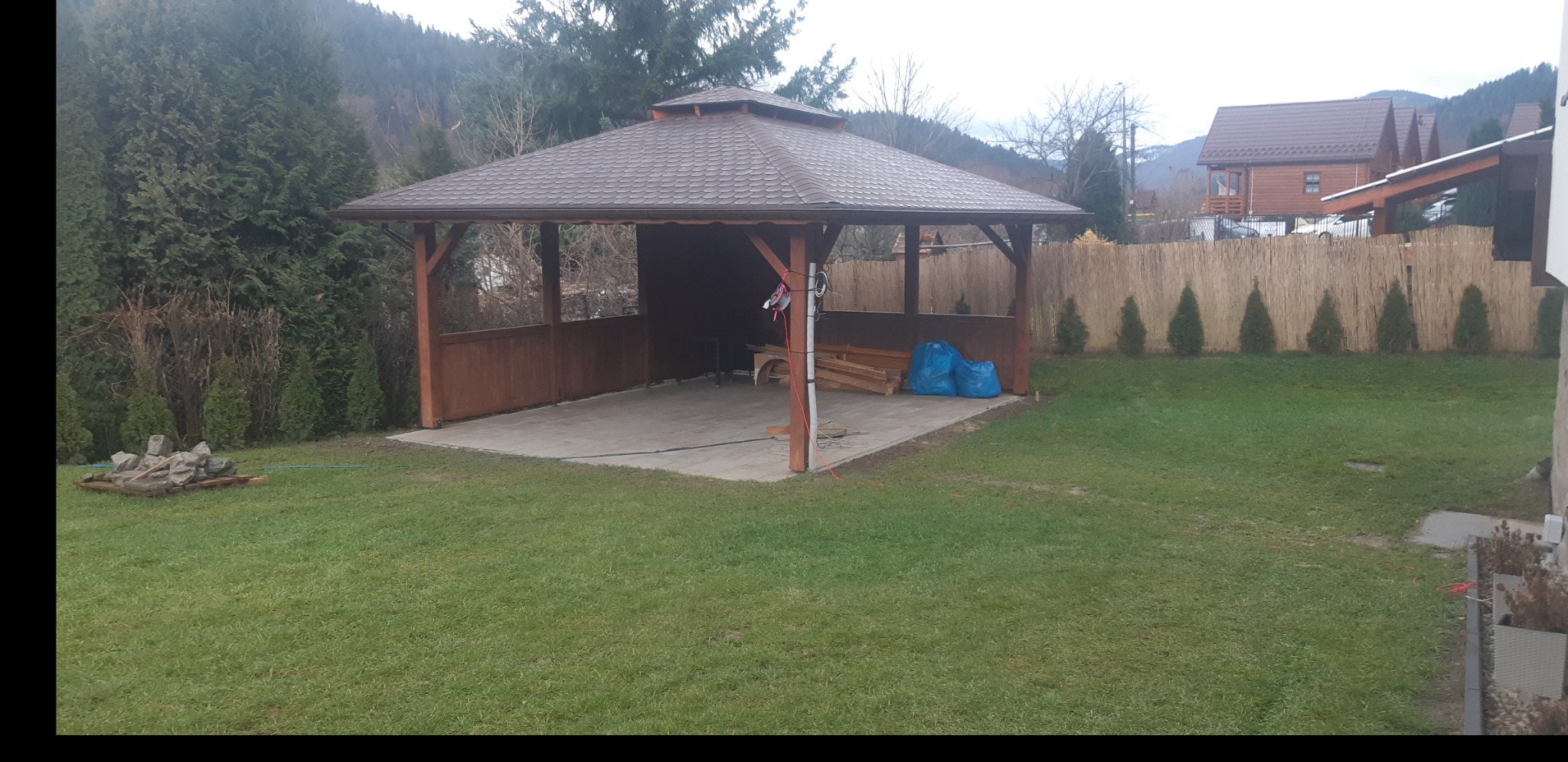 Drewniana konstrukcja z zadaszeniem w Łękawicy, prawdopodobnie altana, z przygotowanym podłożem z kostki, widoczne materiały budowlane i narzędzia na placu budowy.