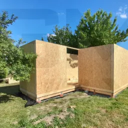 Wznoszenie szkieletu domku letniskowego z płyt OSB na drewnianych legarach, widok z zewnątrz w słoneczny dzień.