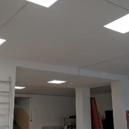 Równomiernie rozmieszczone panele LED w suficie podwieszanym, widoczne okablowanie i drabina w tle, Wałbrzych.