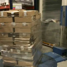 Paleta kartonowych pudeł owinięta folią stretch na obrotowej platformie maszyny do owijania w magazynie.