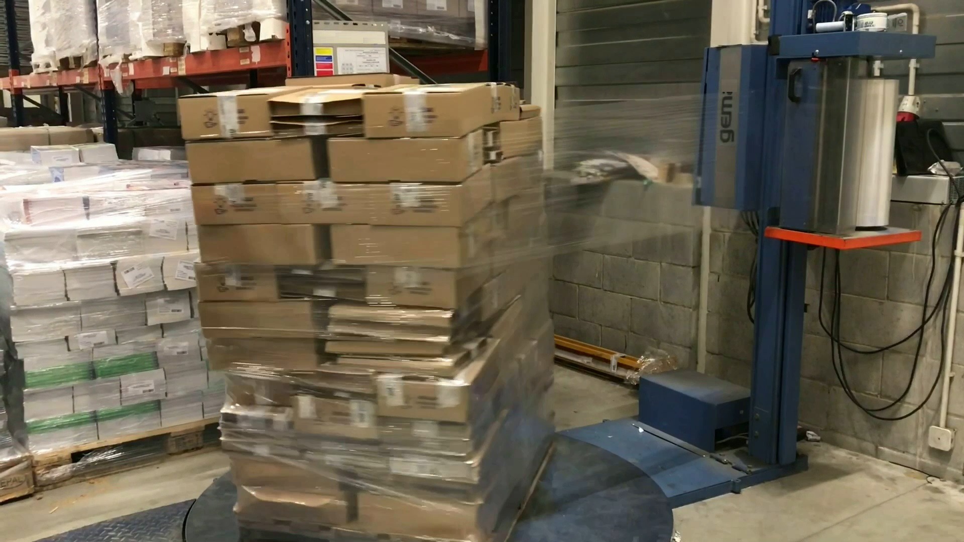 Paleta kartonowych pudeł owinięta folią stretch na obrotowej platformie maszyny do owijania w magazynie.