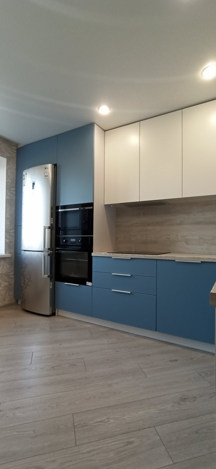 Nowoczesna kuchnia z niebieskimi i białymi szafkami, stalową lodówką LG i drewnopodobną podłogą.