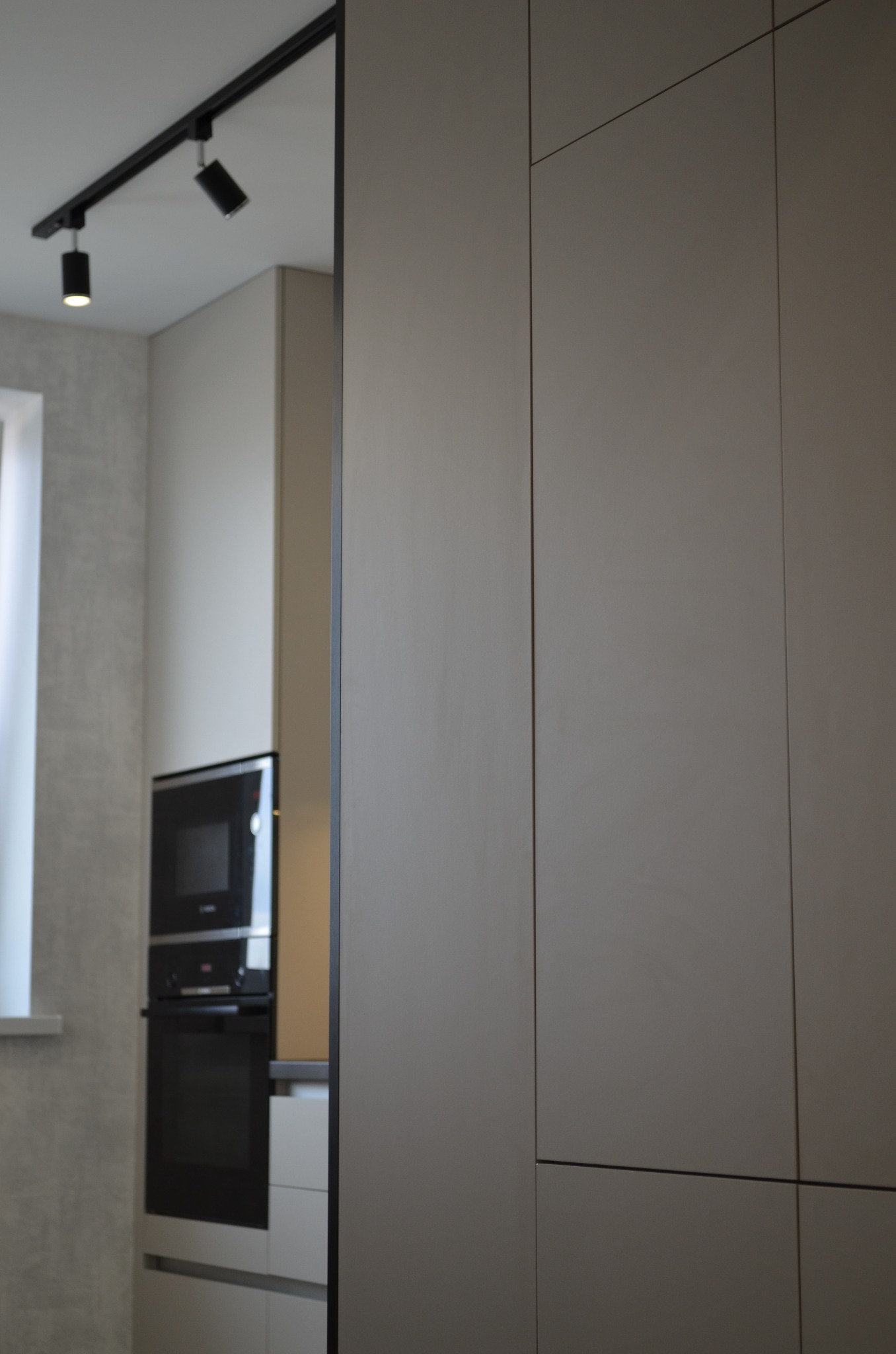 Minimalistyczna kuchnia w odcieniach szarości, z zabudową szafek z frontami bez uchwytów, oświetleniem szynowym i sprzętem AGD w zabudowie.