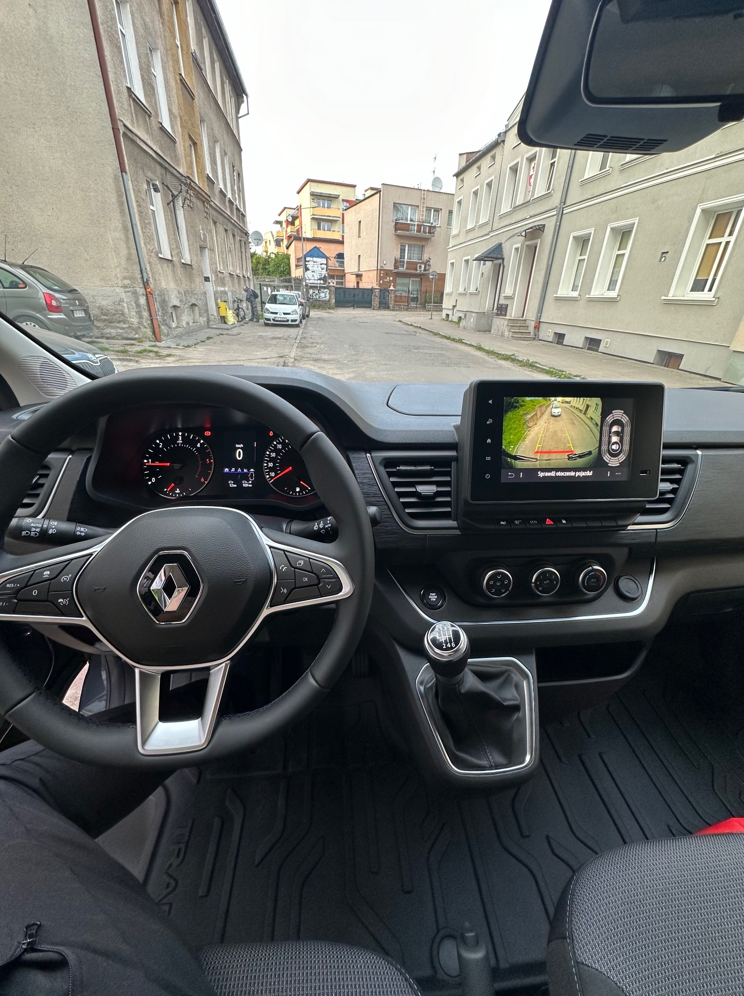 Wnętrze busa Renault z widokiem na ulicę przez przednią szybę i włączony system wspomagania parkowania na ekranie nawigacji.