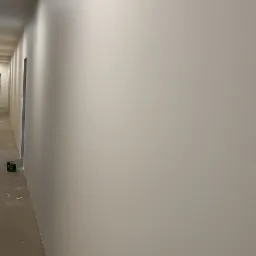 Świeżo pomalowany korytarz z widoczną puszką farby przy ścianie i śladami farby na podłodze.