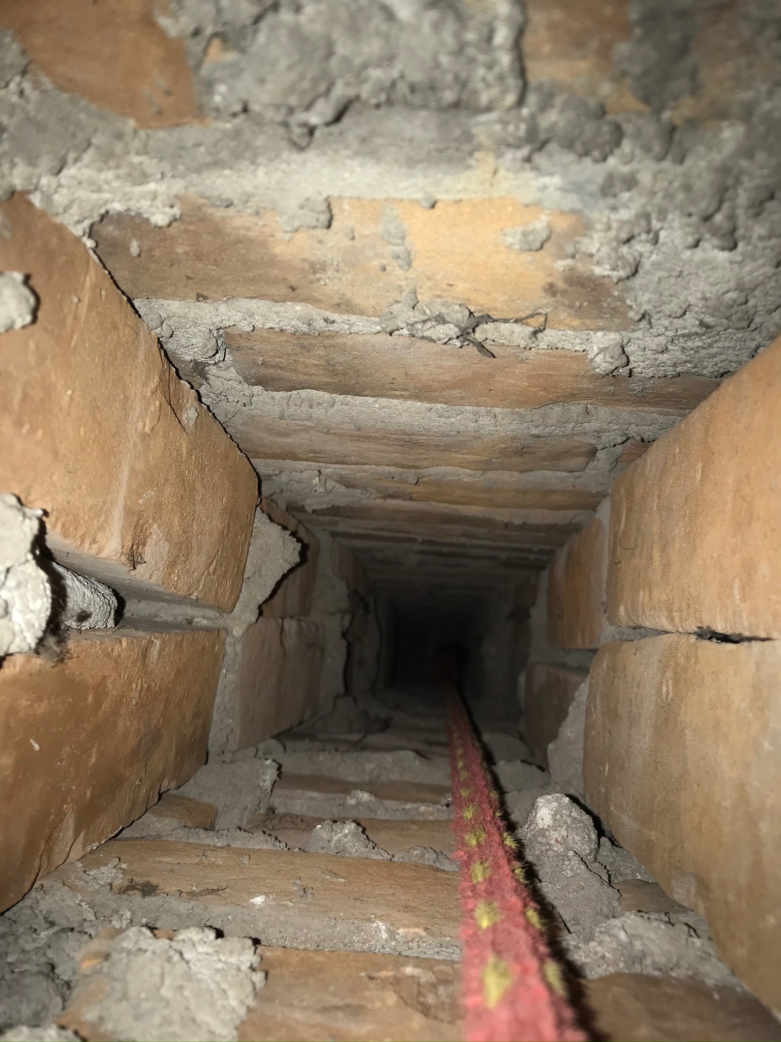 Wnętrze ceglanego przewodu kominowego widziane z dołu, z widoczną czerwoną liną zwisającą w dół.