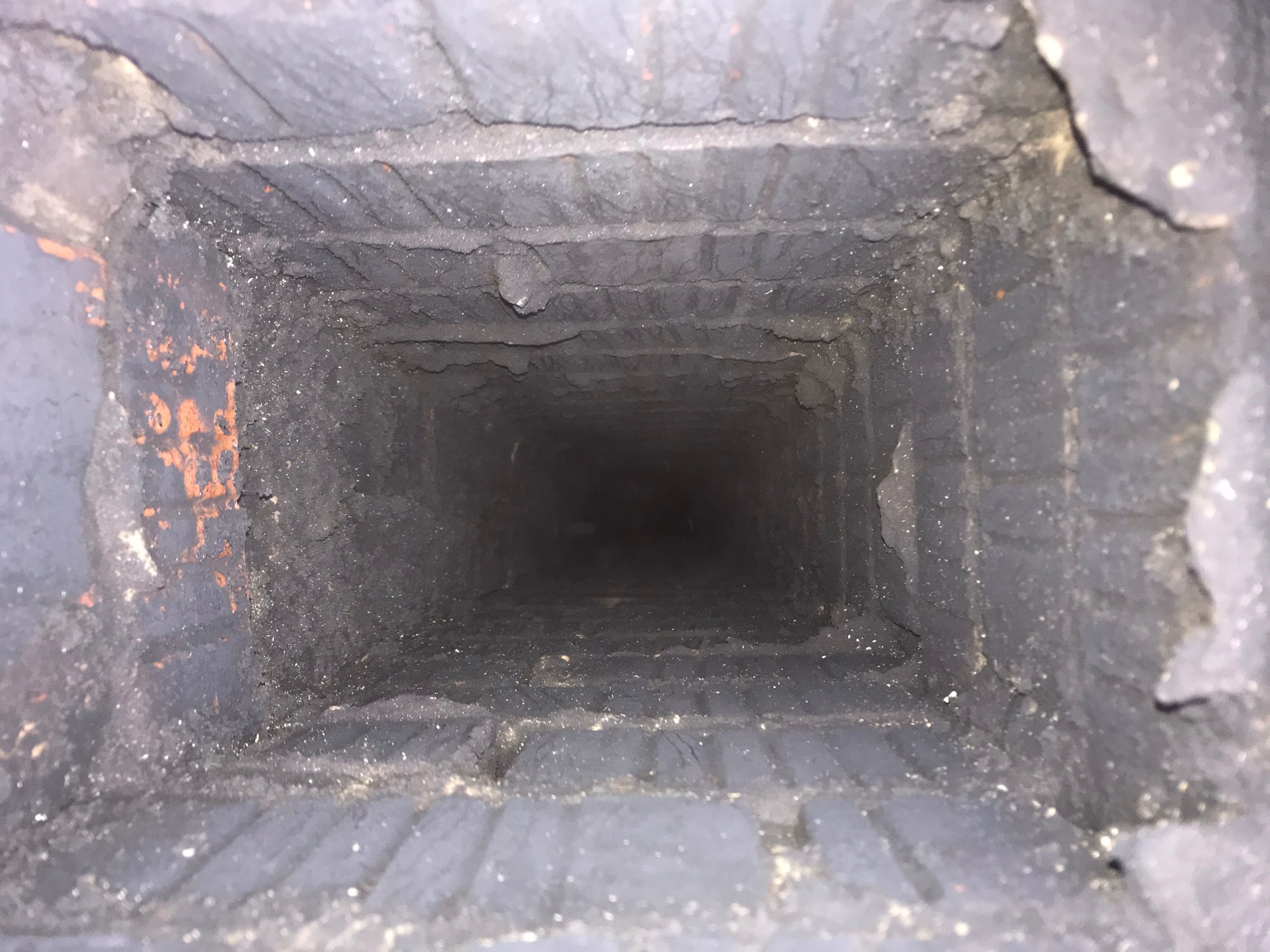 Wnętrze komina z widocznymi osadami sadzy na cegłach, sfotografowane od dołu w górę.