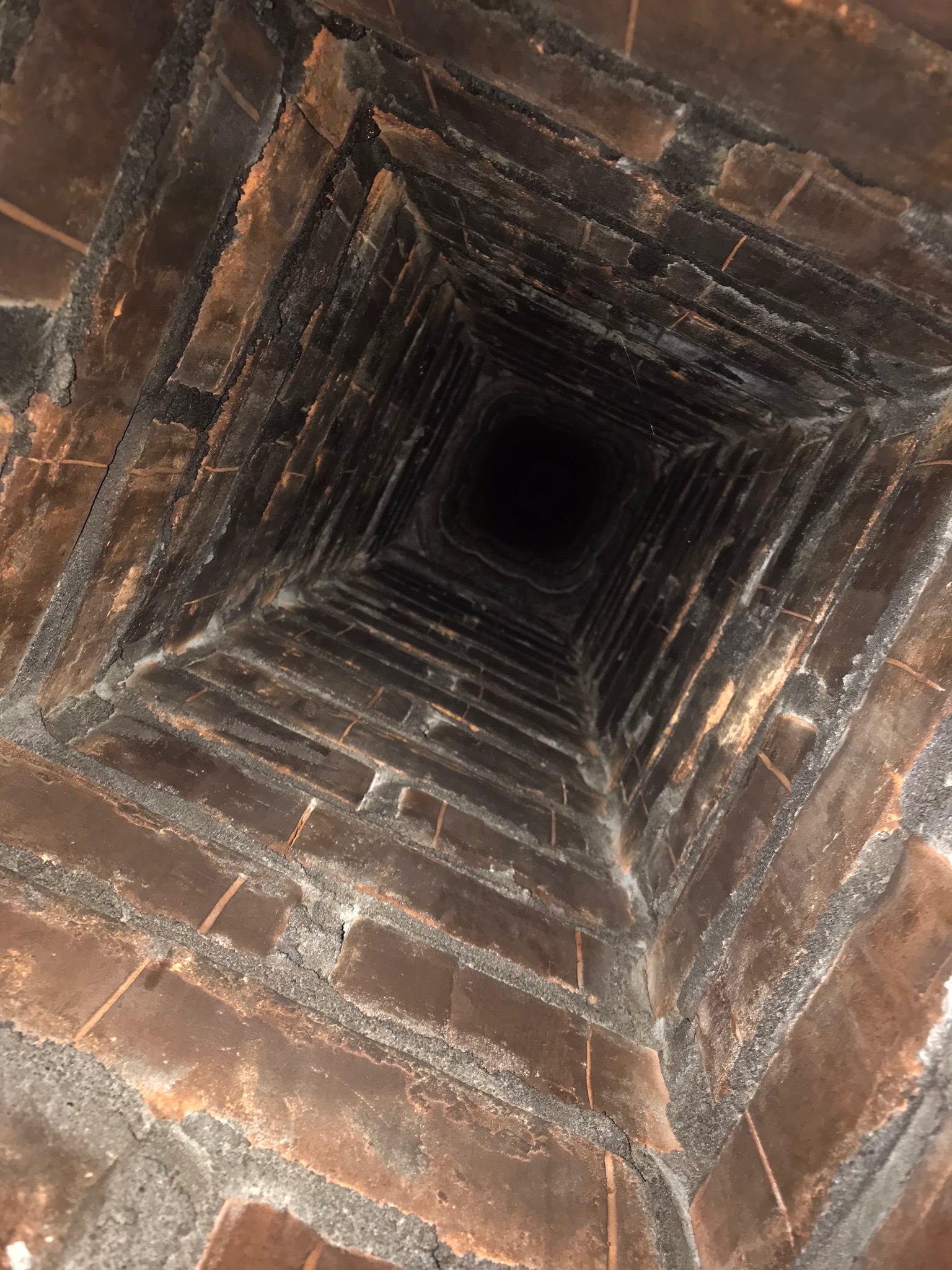 Wnętrze komina z cegły, widok z dołu ku górze, ciemne ślady sadzy na cegłach.