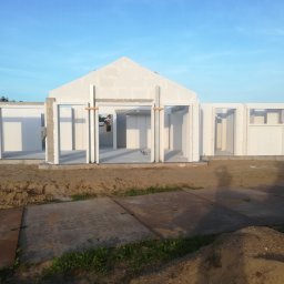 Robert Popiela - Wznoszenie ścian domu z betonu komórkowego Ytong, widoczne otwory okienne i drzwiowe, drewniane stemple podtrzymujące nadproża, w tle błękitne niebo.