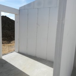 Robert Popiela - Wnętrze budynku w stanie surowym, ściany z białych bloczków, widoczny betonowy fundament i nasyp ziemi za oknem.