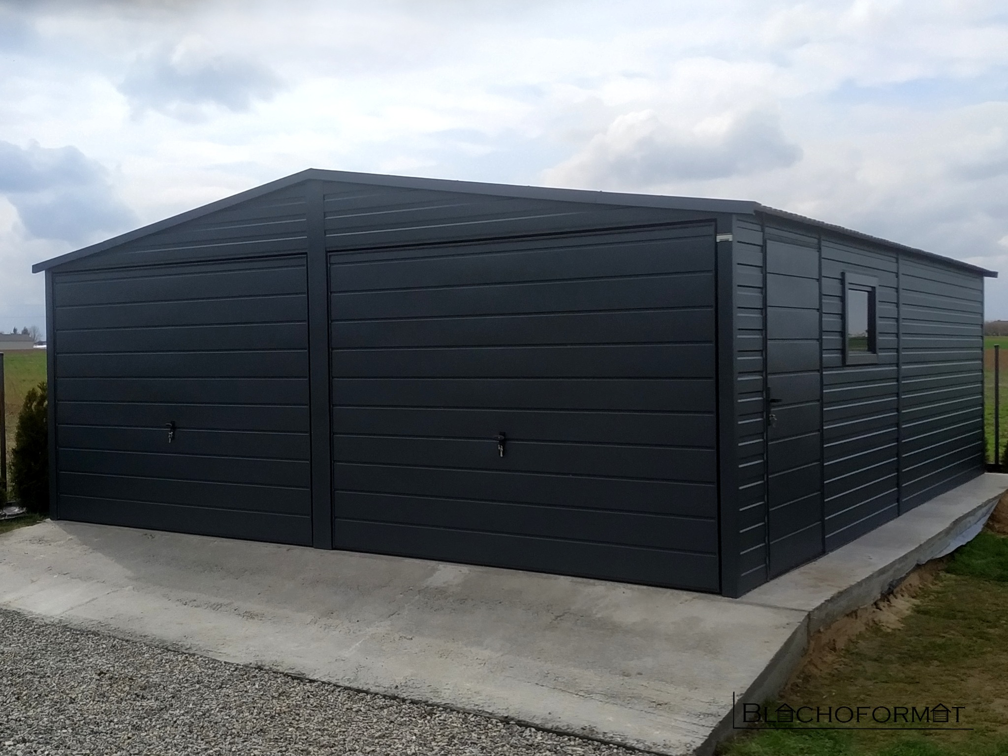 Dwustanowiskowy, ciemnoszary garaż blaszany z oknem bocznym, umieszczony na betonowej wylewce.