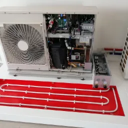 Przekrój pompy ciepła z widocznymi elementami wewnętrznymi, takimi jak sprężarka, wymiennik ciepła i elektronika, umieszczonej na czerwonej platformie z rurami.