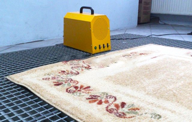 Beżowy dywan z kwiatowym wzorem na metalowej kratce, obok żółte urządzenie z uchwytem i pokrętłami.