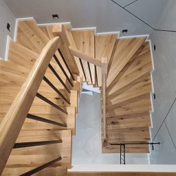 Kamil Sokalski - Spiralne schody dębowe z czarnymi balustradami, widok z góry, oświetlenie punktowe. Realizacja w Rawiczu. Unikalny design, nowoczesne wykończenie.