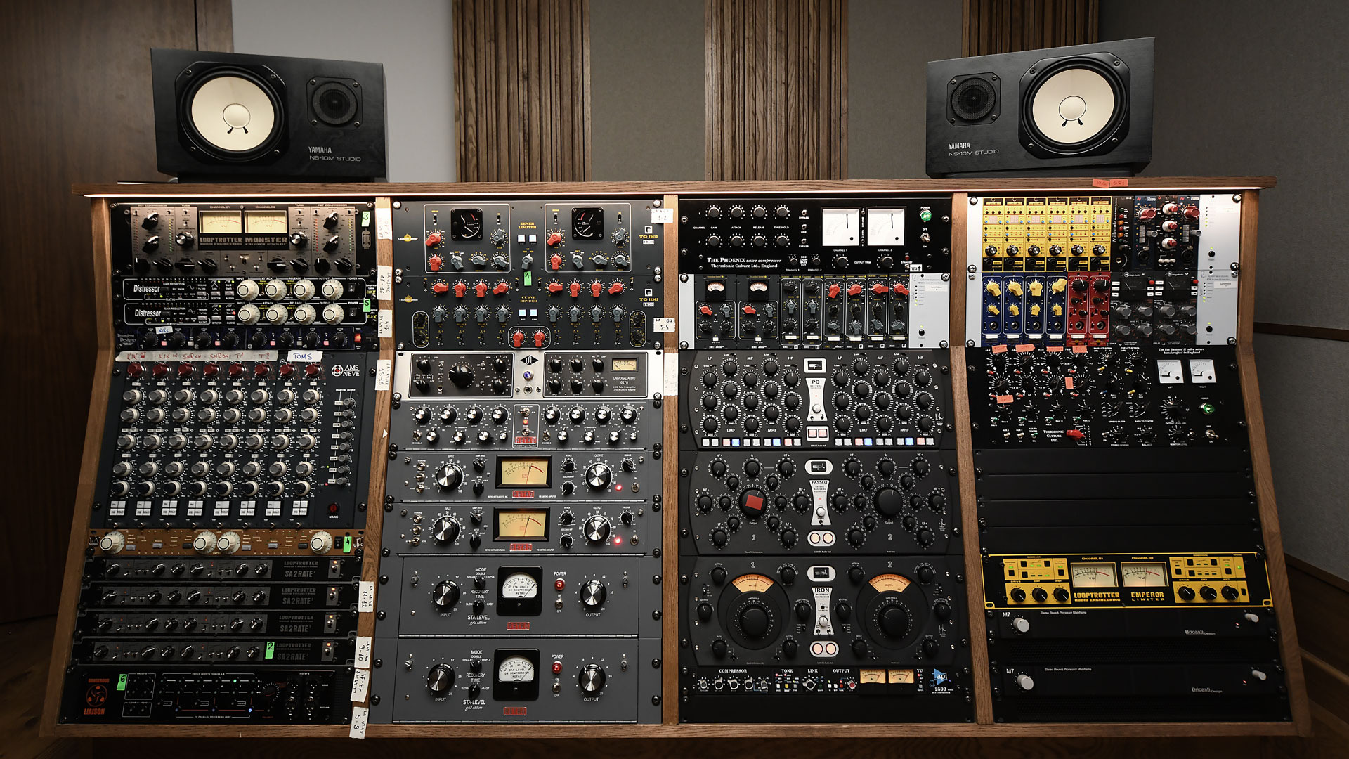 Rząd studyjnych procesorów dźwięku i mikserów w drewnianej obudowie, zwieńczony głośnikami Yamaha NS-10M Studio, widok z przodu.