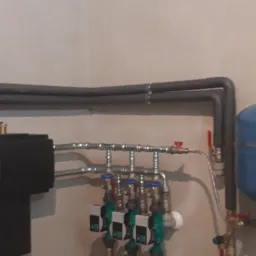 Rozdzielacz instalacji centralnego ogrzewania z czterema obiegami grzewczymi, każdy wyposażony w pompę obiegową, zamontowany na ścianie w kotłowni.