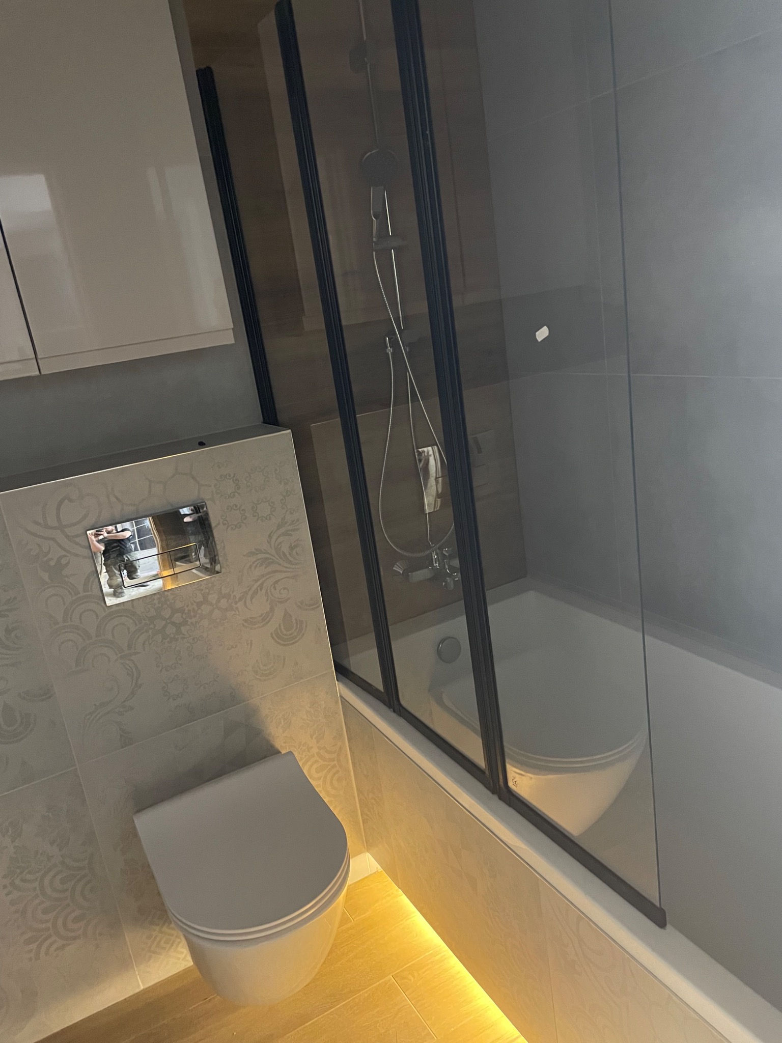 Nowoczesna łazienka z kabiną prysznicową typu walk-in z czarnymi profilami, wiszącą miską WC i ozdobnymi płytkami na ścianach.