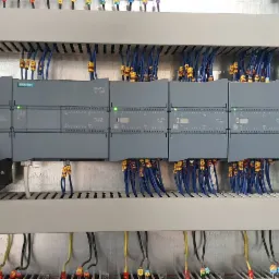 Rozdzielnica elektryczna z modułami sterującymi Siemens, widoczne okablowanie i diody sygnalizacyjne, całość zamontowana w szafie rack.