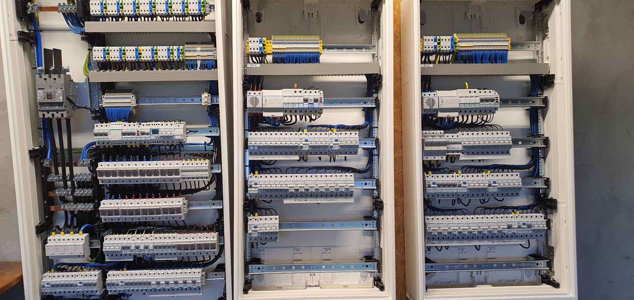 Trzy rozdzielnice elektryczne w białych obudowach, widoczne liczne bezpieczniki, przewody i listwy zaciskowe, starannie ułożone i podłączone, z różnymi oznaczeniami i numeracjami.