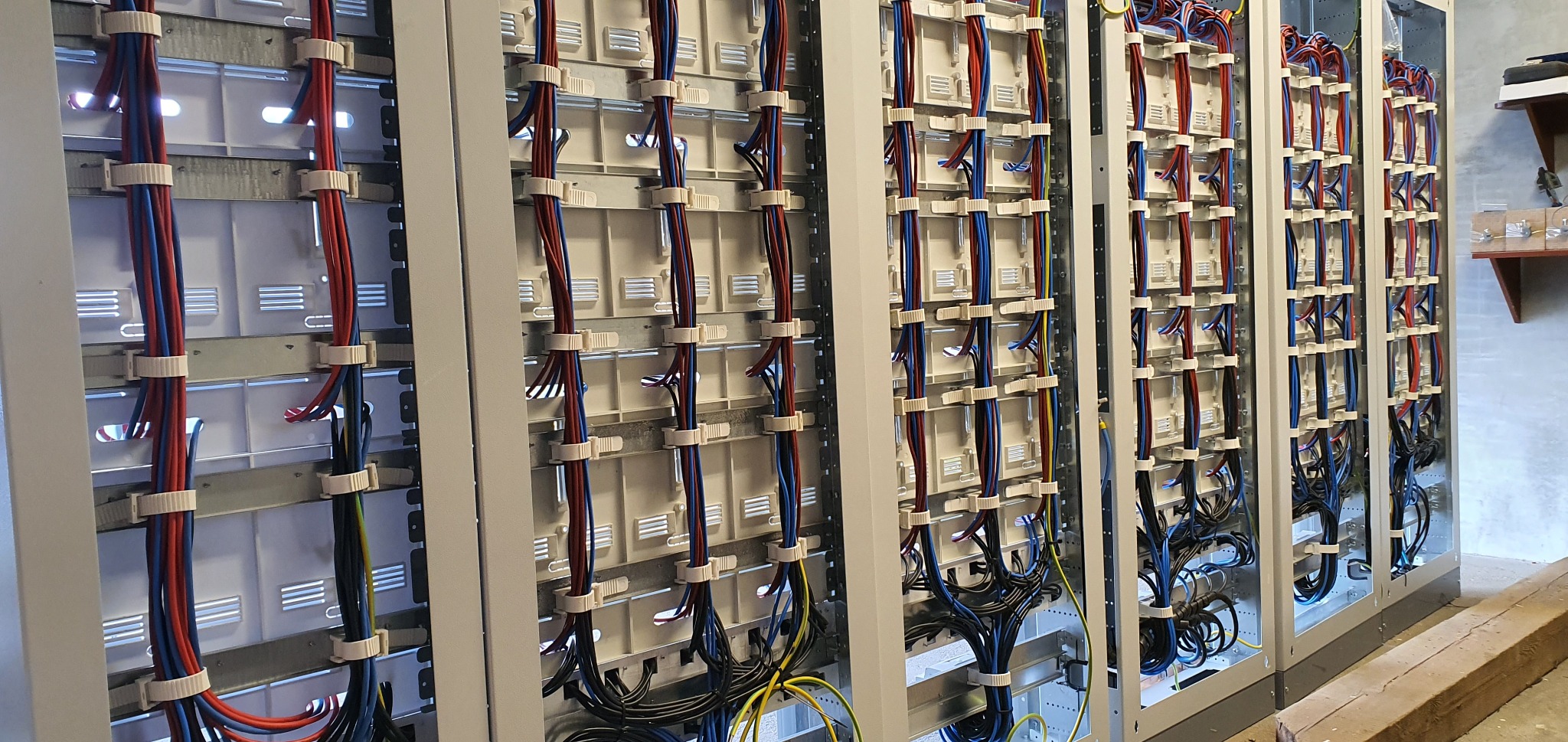 Rozdzielnica elektryczna z uporządkowanymi przewodami w kolorach niebieskim, czerwonym i czarnym, zamocowanymi za pomocą białych uchwytów kablowych.