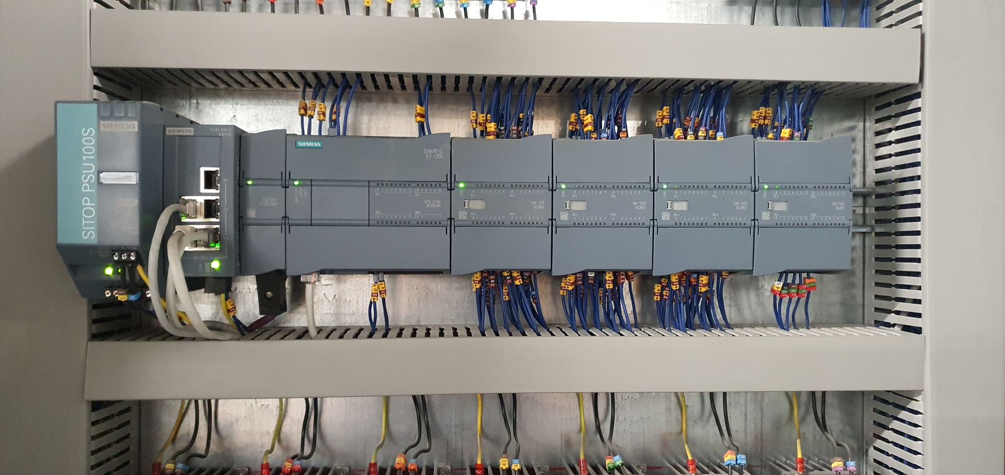 Rozdzielnica elektryczna z modułami sterującymi Siemens, widoczne okablowanie i diody sygnalizacyjne, całość zamontowana w szafie rack.