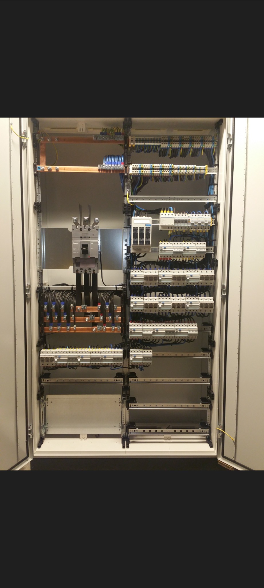 Otwarta szafa elektryczna z widocznymi zabezpieczeniami, przewodami i szynami, uporządkowana instalacja w kolorach niebieskim, żółtym i czarnym.