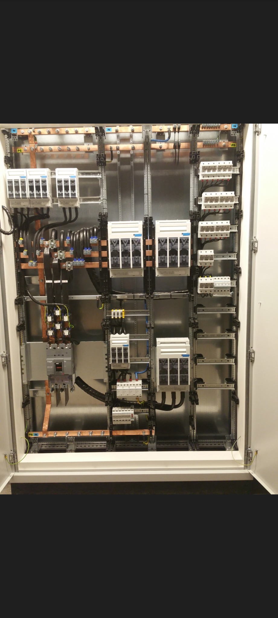 Otwarta szafa elektryczna z widocznymi bezpiecznikami, przewodami i szynami montażowymi, uporządkowana instalacja w metalowej obudowie.