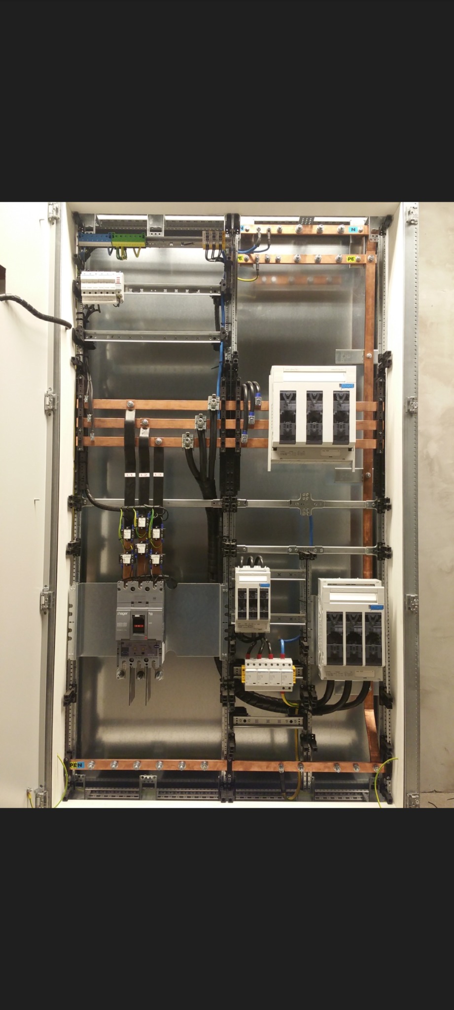 Wnętrze rozdzielnicy elektrycznej z zainstalowanymi zabezpieczeniami, szynami miedzianymi i okablowaniem, widoczne elementy montażowe i złącza.