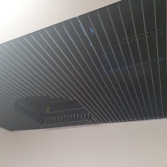 Czarny, rastrowy sufit podwieszany z widoczną instalacją oświetleniową, zamontowany w pomieszczeniu o jasnych ścianach.