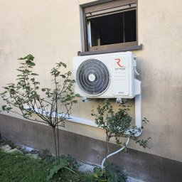 KajMar Arkadiusz Rutkowski - Biały klimatyzator Rotenso zamontowany na elewacji domu pod oknem, z widoczną instalacją odprowadzającą skropliny, otoczony zielenią. Ujęcie z dołu.