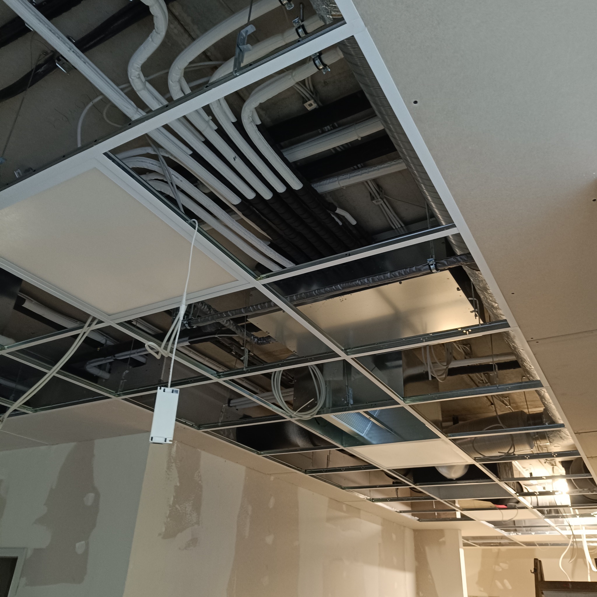Sufit podwieszany z widoczną instalacją klimatyzacji i wentylacji w trakcie montażu. Widoczne rury, kable i elementy konstrukcyjne.