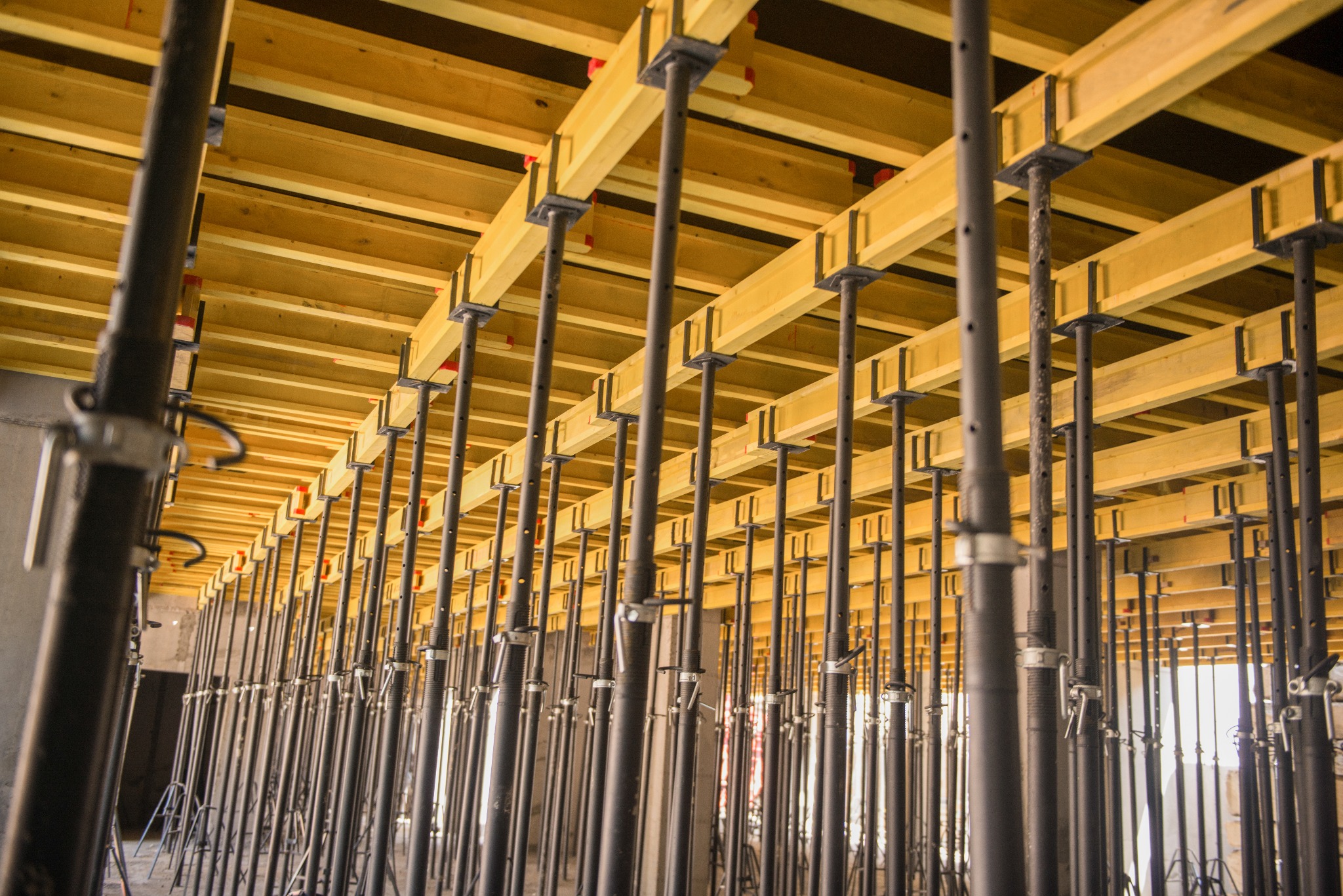Szczegółowe ujęcie szalunku stropowego z drewnianymi belkami i metalowymi podporami, widoczne z dołu, w trakcie budowy.