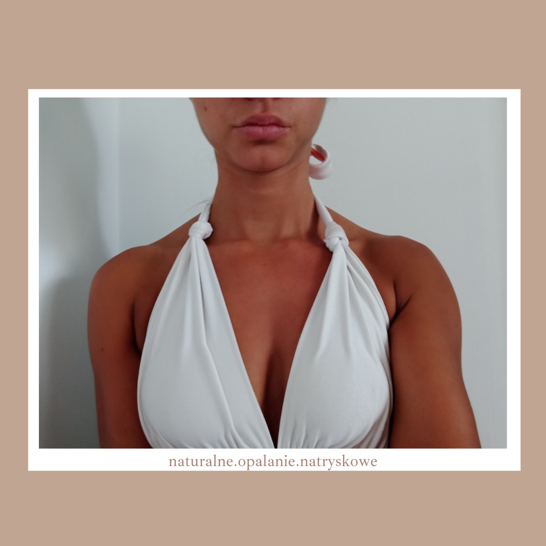 Kobieta z widoczną opalenizną natryskową na dekolcie i ramionach, ubrana w białą sukienkę z wiązanymi ramiączkami.