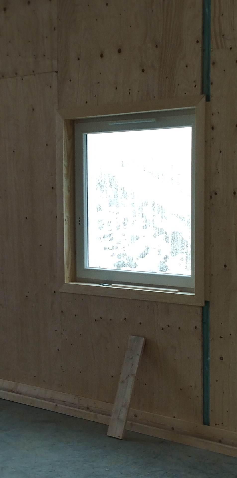 Montaż okna w surowej ścianie z płyty OSB, widoczna listwa przypodłogowa i kawałek deski oparty o ścianę.