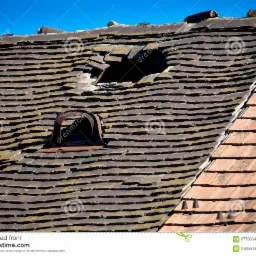 Uszkodzony dach z dziurą i skorodowaną metalową wentylacją w Łodzi, wymagający wymiany dachówek.